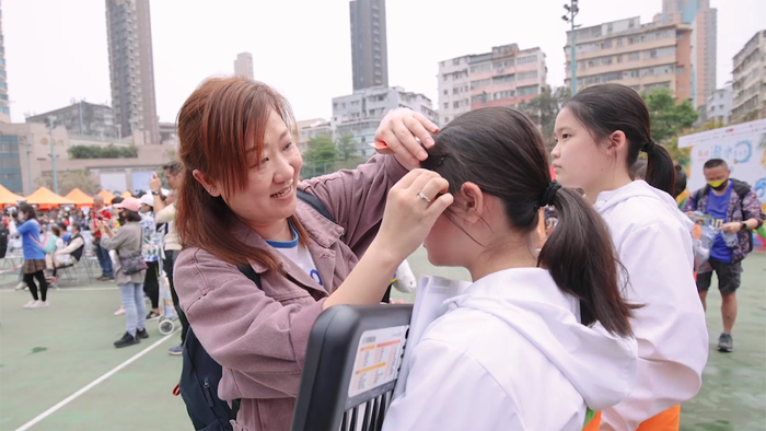「家长义工」吴崇熙妈妈在乐团表演前，细心为团员整理头发。